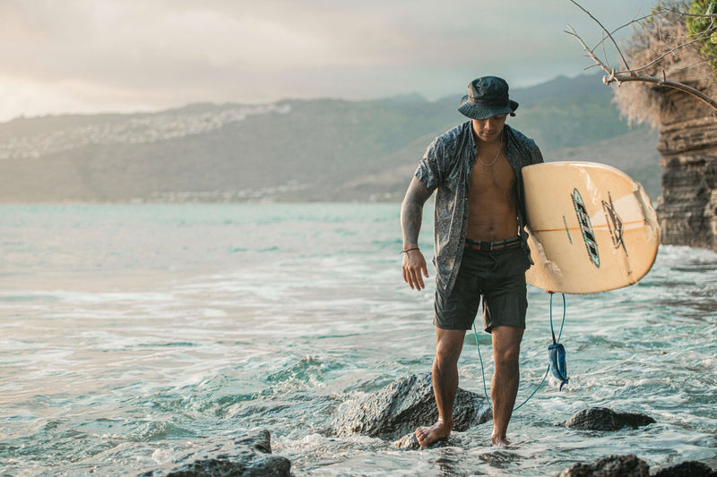 Man holding a surfboard wearing hat and belt