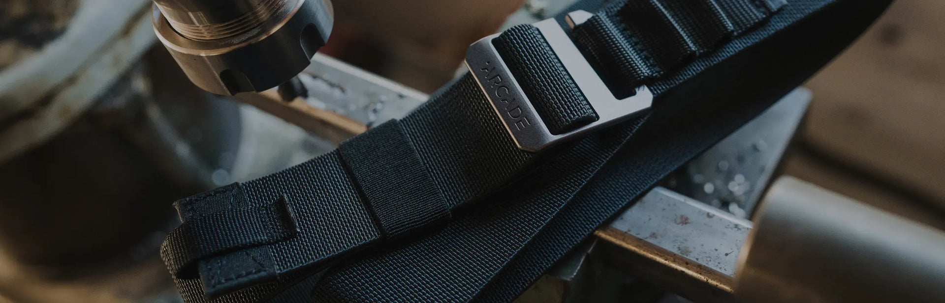 Close-up of two black Arcade brand belts with textured straps and metal buckles, placed parallel on a dark surface.