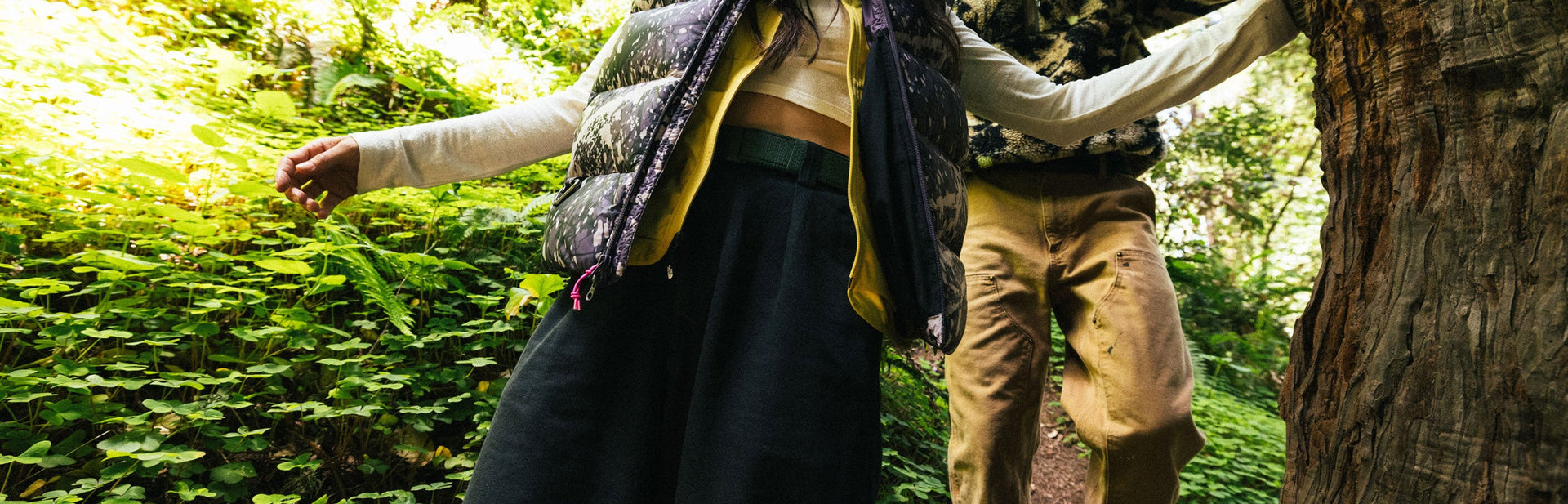 A person wearing tan shorts is caught mid-air while jumping off a rocky cliff, arms and legs extended, against a clear blue sky with hills in the background.