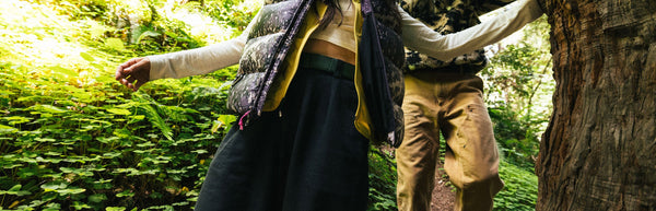 A person wearing tan shorts is caught mid-air while jumping off a rocky cliff, arms and legs extended, against a clear blue sky with hills in the background.