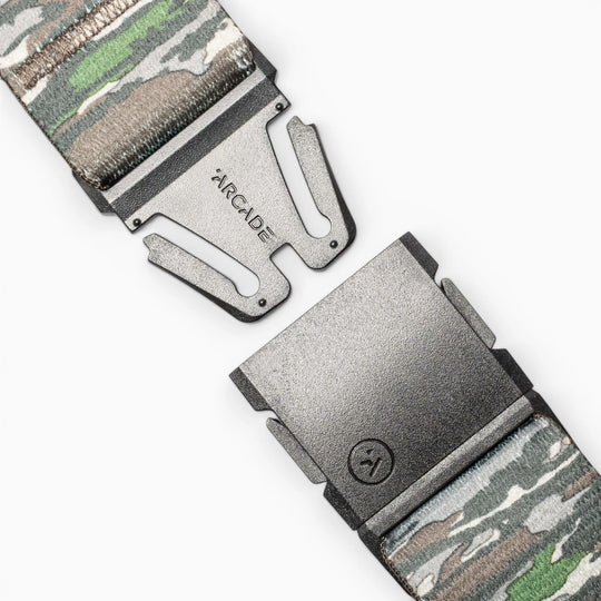 Close-up of the Realtree Camo Original by Arcade Belts, a stretch webbing belt with a camouflage pattern, partially open metal buckle engraved “ARCADE,” and a small lower logo.
