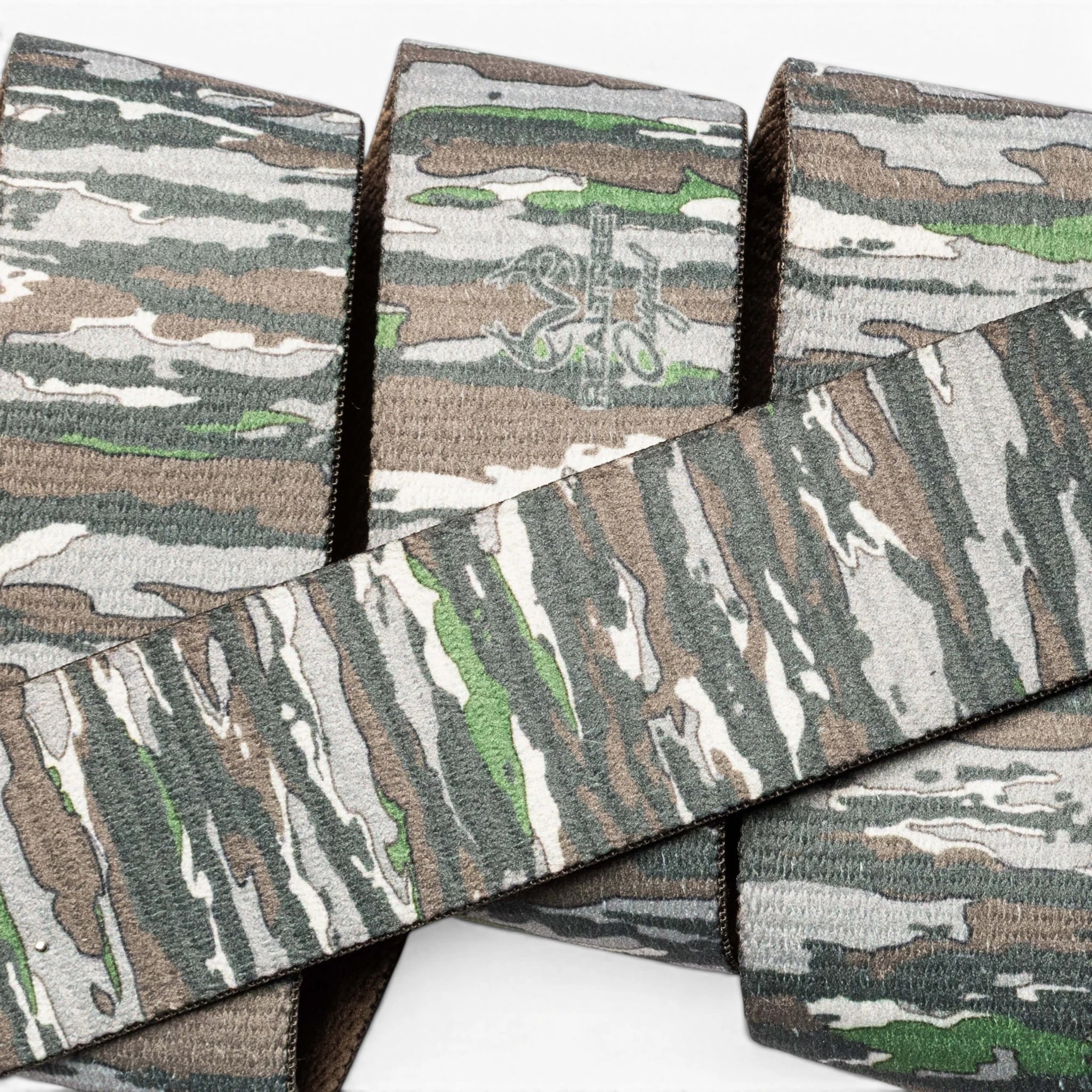 A close-up of Arcade Belts’ Realtree Camo Original, featuring stretch webbing with fabric straps in green, brown, tan, and gray camouflage overlapping against a white background.