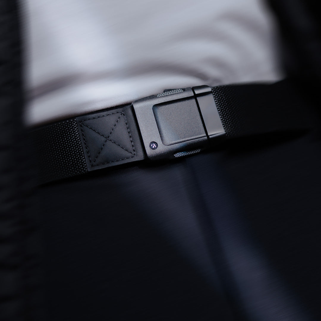 Close-up of a person wearing a low profile belt with a modern, rectangular buckle over dark pants and a white shirt. The focus is on the belt buckle, highlighting its sleek, minimalist design perfect for travel or everyday wear.