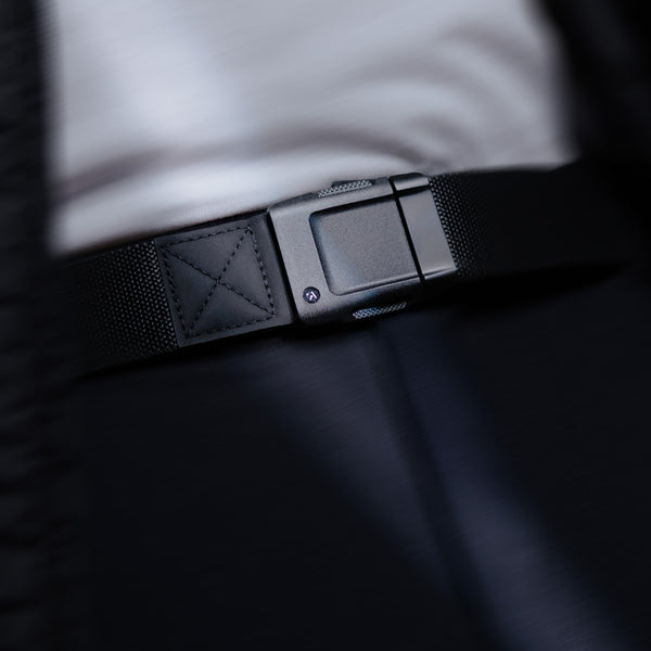 Close-up of a person wearing a low profile belt with a modern, rectangular buckle over dark pants and a white shirt. The focus is on the belt buckle, highlighting its sleek, minimalist design perfect for travel or everyday wear.