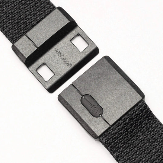 Close-up of the Aero belt by Arcade Belts—a black, durable belt with a rectangular plastic buckle featuring SwiftLock technology, two square holes, a button mechanism, and "ARCADE" text visible against a white background.