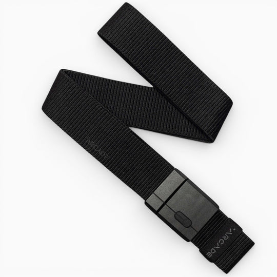 A black Mag Kit II woven nylon stretch belt by Arcade Belts, featuring a rectangular black plastic buckle, is displayed on a white background. The belt is partially folded, showcasing its flexible texture and modern minimalist design that exemplifies the adventurous spirit of Arcade Belts.