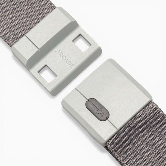 A close-up of the Aero Mag belt by Arcade Belts, highlighting its gray fabric strap and rectangular plastic buckle. The buckle showcases the word “ARCADE” and features a small button with a lock icon for quick release. Built with SwiftLock technology, this durable buckle ensures effortless fastening and added security.
