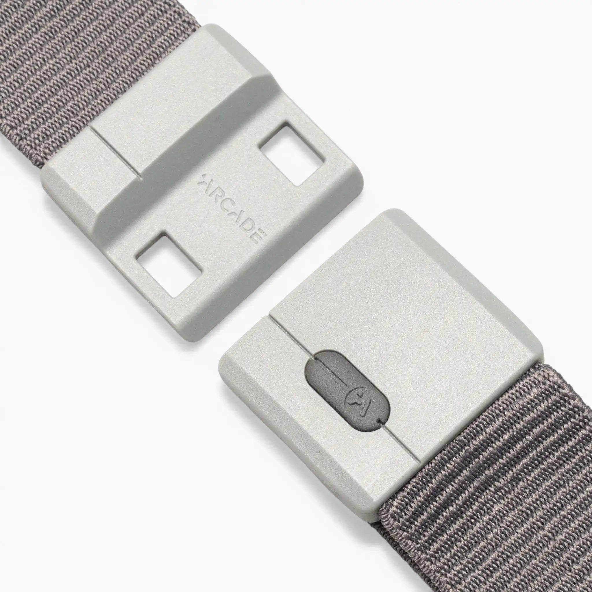 A close-up of the Aero Mag belt by Arcade Belts, highlighting its gray fabric strap and rectangular plastic buckle. The buckle showcases the word “ARCADE” and features a small button with a lock icon for quick release. Built with SwiftLock technology, this durable buckle ensures effortless fastening and added security.
