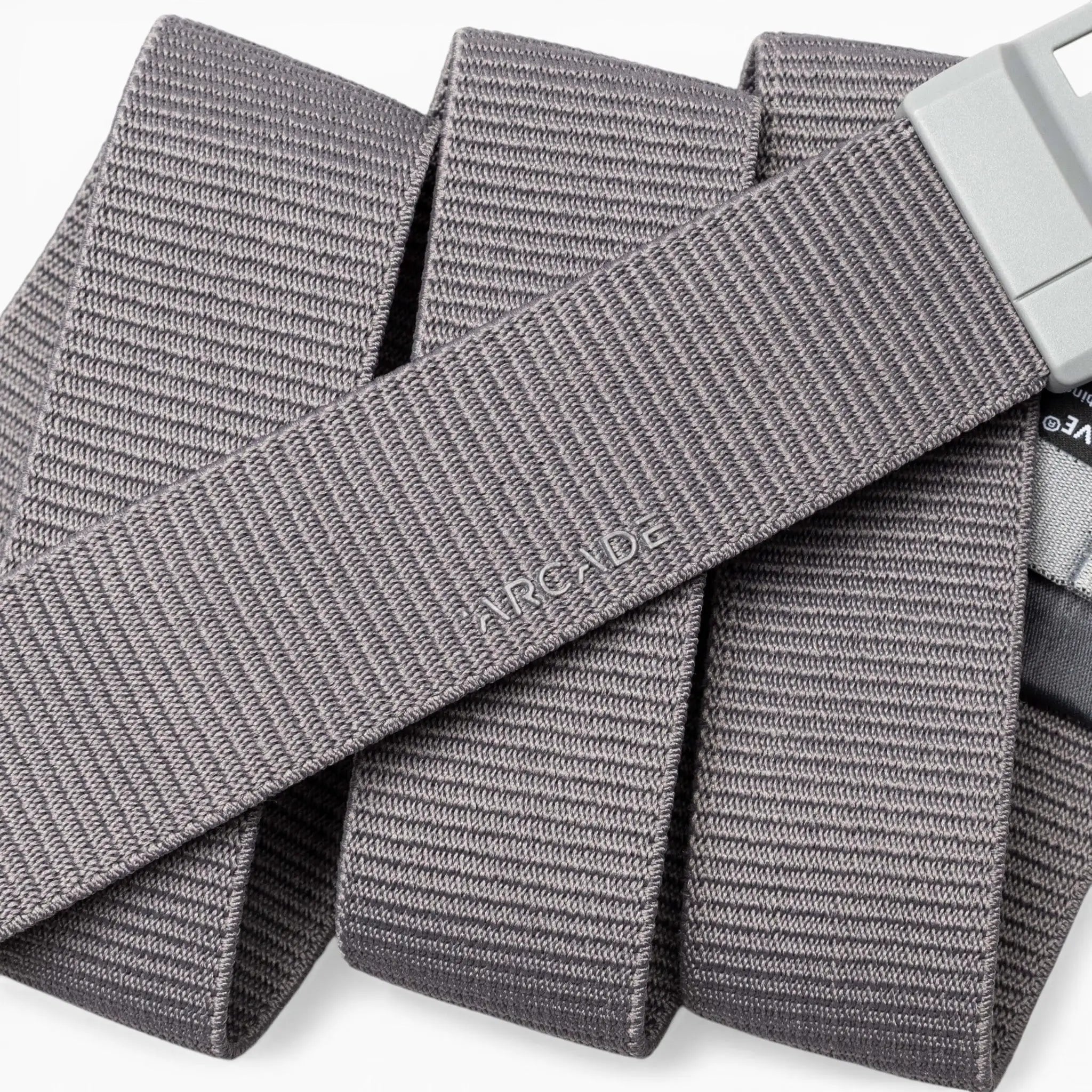 A close-up of a gray, textured Aero Mag belt by Arcade Belts with a durable metal buckle. The word “ARCADE” is embossed on the belt, which is arranged in overlapping folds.
