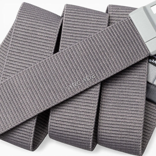 A close-up of a gray, textured Aero Mag belt by Arcade Belts with a durable metal buckle. The word “ARCADE” is embossed on the belt, which is arranged in overlapping folds.