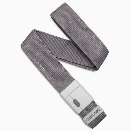 A gray fabric stretch belt, the Mag Kit II by Arcade Belts, features a rectangular SwiftLock buckle and displays the Arcade logo near the buckle. The belt is coiled in a loose spiral, highlighting the quality and innovative design of Arcade Belts products.