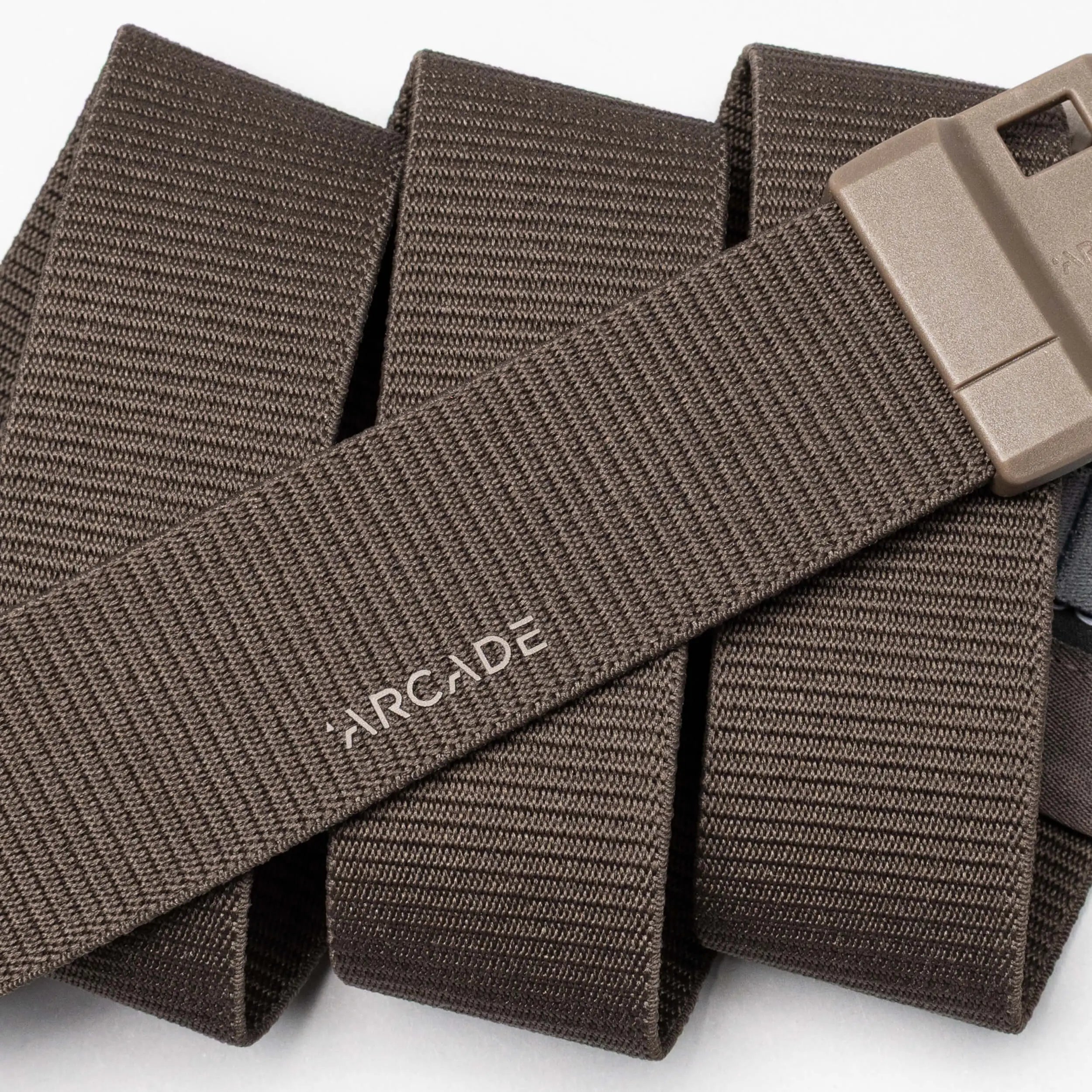 A close-up of the Aero belt by Arcade Belts: a brown, durable belt with textured lines, "ARCADE" in white, and a rectangular tan plastic buckle. Features SwiftLock technology for easy fastening.