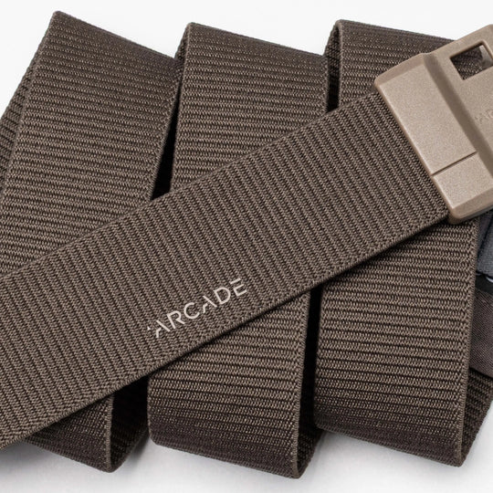 A close-up of the Aero belt by Arcade Belts: a brown, durable belt with textured lines, "ARCADE" in white, and a rectangular tan plastic buckle. Features SwiftLock technology for easy fastening.
