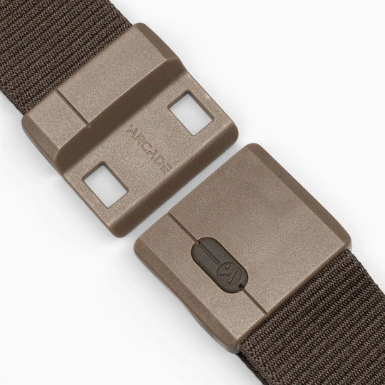 A close-up of the Aero Mag, a brown plastic belt buckle by Arcade Belts featuring a sliding tension lock mechanism, attached to a textured brown fabric strap. The durable buckle is partially opened, displaying the Arcade logo on one side.