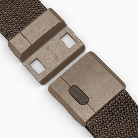 A close-up of the Aero Mag, a brown plastic belt buckle by Arcade Belts featuring a sliding tension lock mechanism, attached to a textured brown fabric strap. The durable buckle is partially opened, displaying the Arcade logo on one side.
