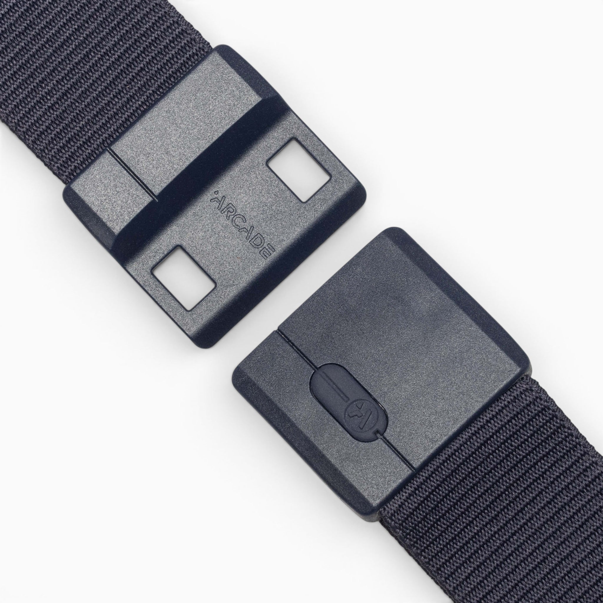 A close-up of the Aero Mag belt by Arcade Belts shows a black fabric strap with a durable buckle, partially unfastened, displaying the word "ARCADE" on one side. The buckle is equipped with two square holes, a locking mechanism, and features a tension lock for secure fastening.