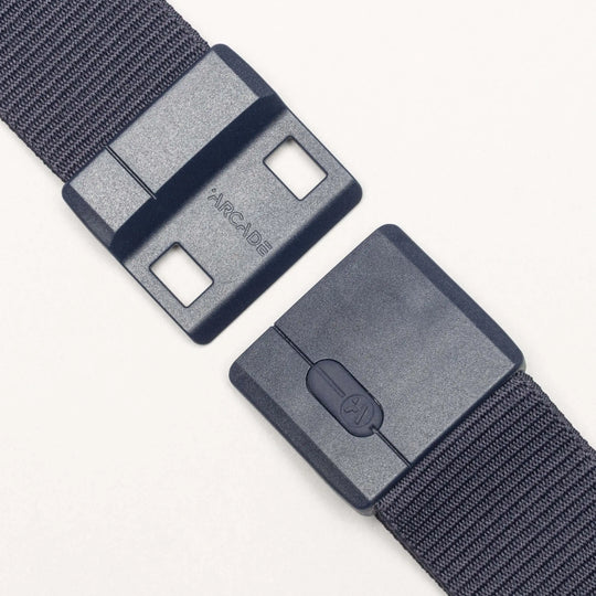 A close-up of the Aero adjustable fabric belt from Arcade Belts in dark gray, featuring a durable rectangular buckle. The unfastened buckle displays its two interlocking parts against a light background.