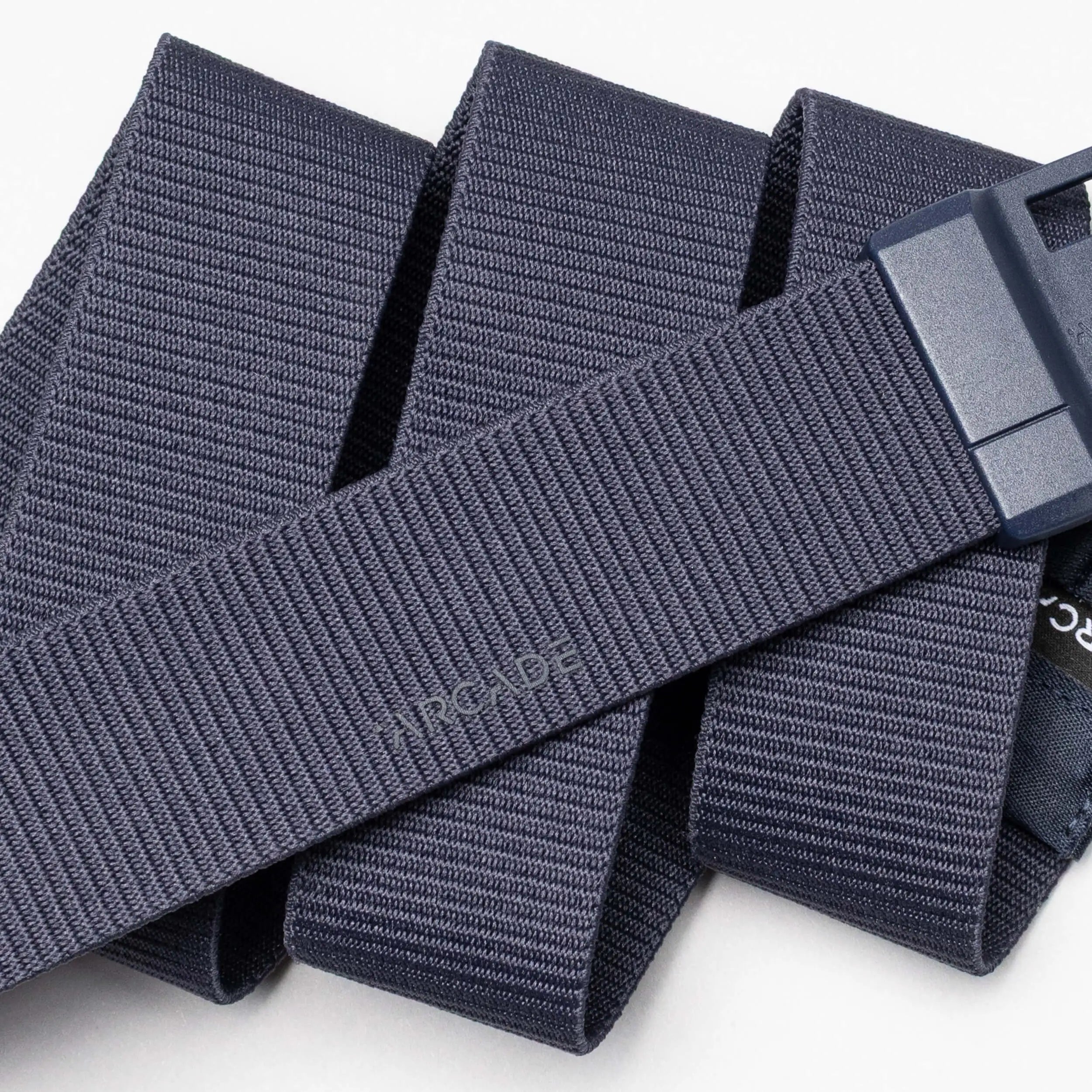 A close-up of the Aero Mag by Arcade Belts, a navy blue fabric belt with a durable buckle, neatly folded in overlapping layers on a white background.
