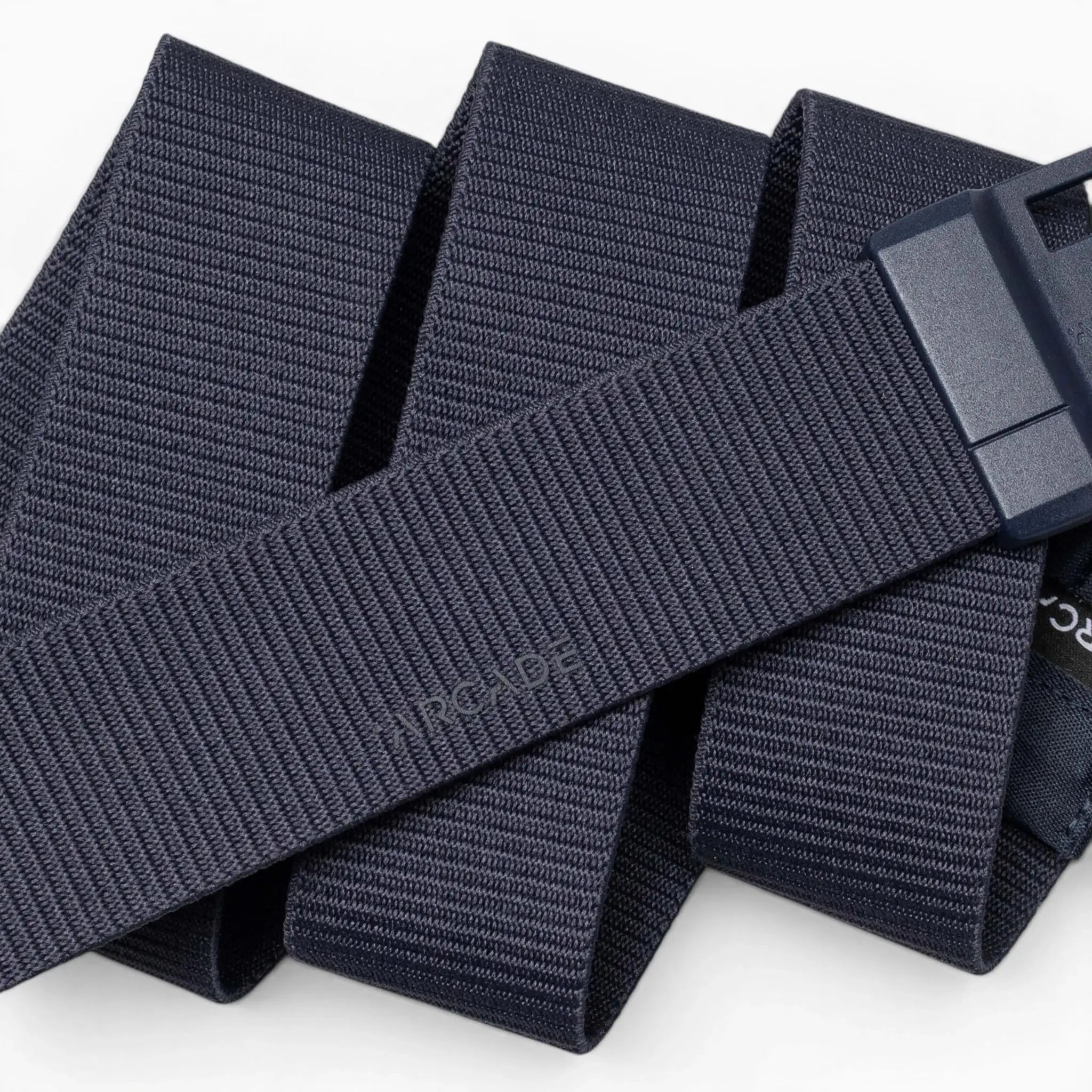 A close-up photo of the Aero Mag belt by Arcade Belts in navy blue, featuring a textured woven design and a durable rectangular buckle, displayed in overlapping, folded sections against a white background.
