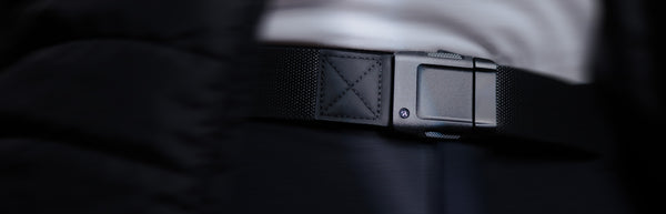 Close-up of a person wearing an Arcade Belt, featuring a matte, rectangular buckle. The low profile belt is paired with dark pants and a white shirt, with the image softly blurred around the edges to highlight the belt and buckle.