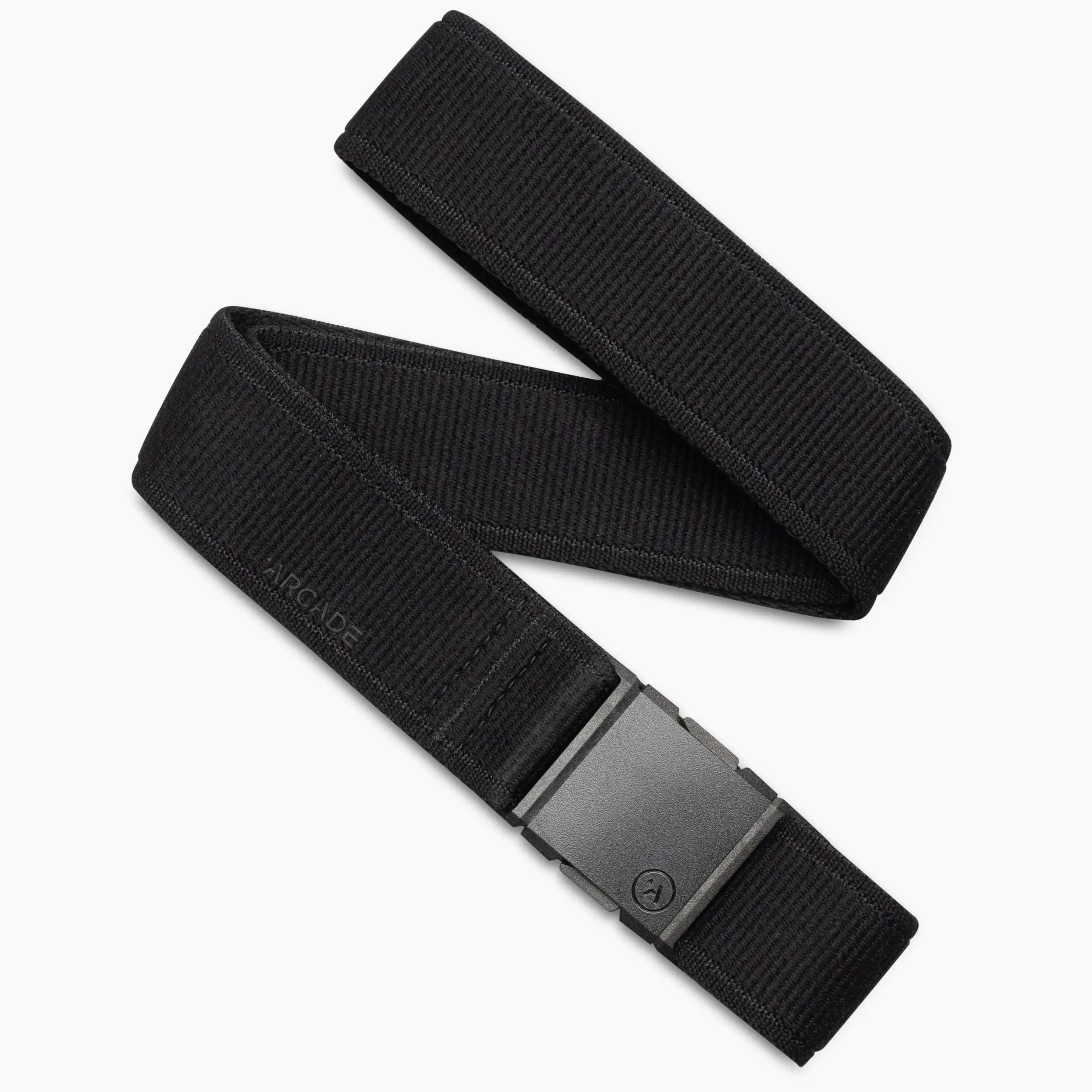 The Atlas Kit by Arcade Belts is a black stretch webbing belt with a matte black rectangular buckle, shown coiled on a white background. ARCADE is subtly embossed near the buckle—ideal for those seeking stylish travel belts.