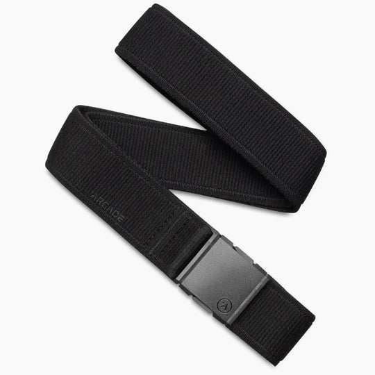 The Atlas Kit by Arcade Belts is a black stretch webbing belt with a matte black rectangular buckle, shown coiled on a white background. ARCADE is subtly embossed near the buckle—ideal for those seeking stylish travel belts.