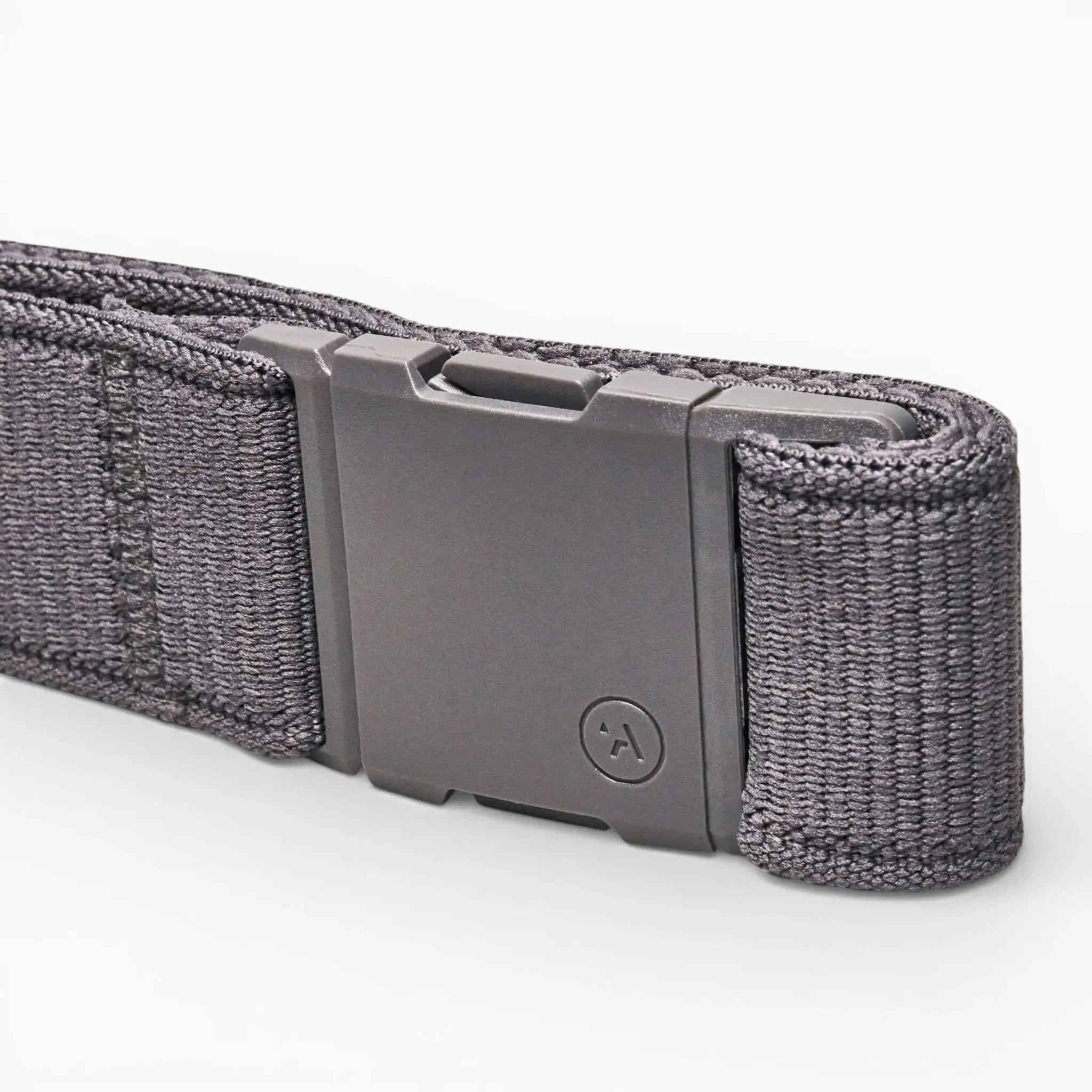 A close-up of an Arcade Belts Atlas dark gray woven Elastic Stretch Belt with a rectangular matte gray, low-profile buckle featuring a circular logo with an upward-pointing arrow, resting on a light background.