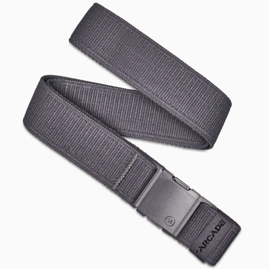 The Atlas by Arcade Belts is a dark gray low-profile belt with a rectangular plastic buckle, shown coiled on a white background. ARCADE is printed near the buckle, making it perfect for travel or daily use.