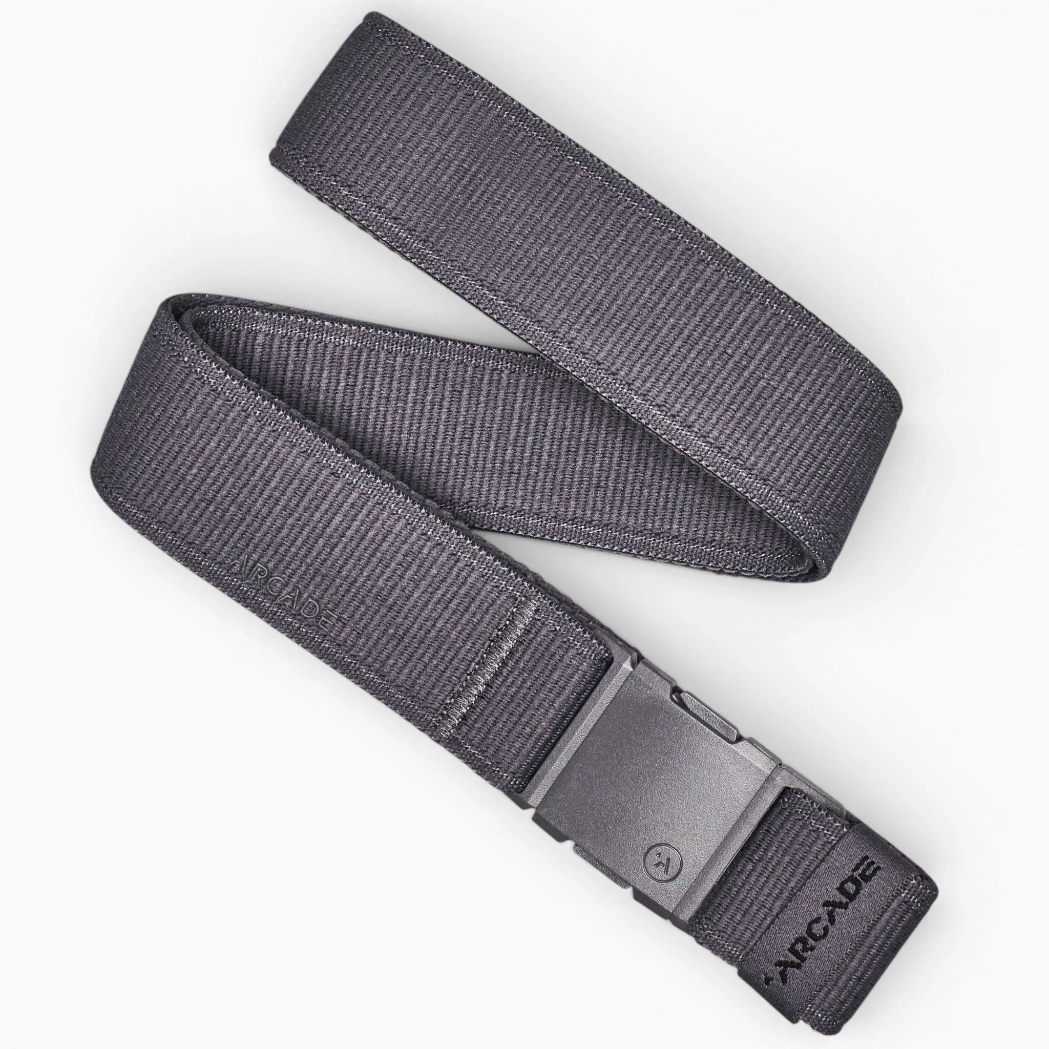 The Atlas by Arcade Belts is a dark gray low-profile belt with a rectangular plastic buckle, shown coiled on a white background. ARCADE is printed near the buckle, making it perfect for travel or daily use.