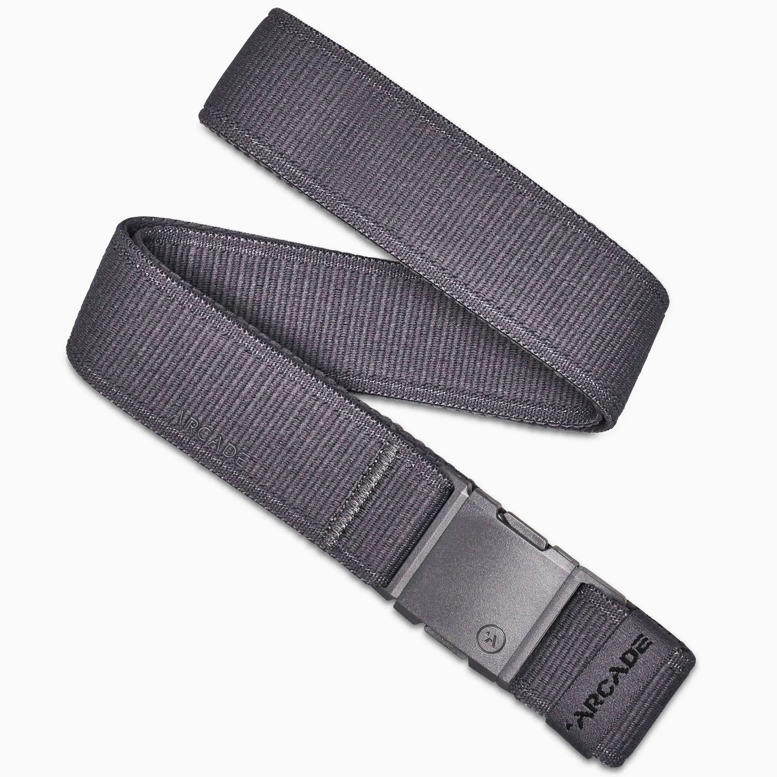 The Atlas by Arcade Belts is a dark gray low-profile belt with a rectangular plastic buckle, shown coiled on a white background. ARCADE is printed near the buckle, making it perfect for travel or daily use.