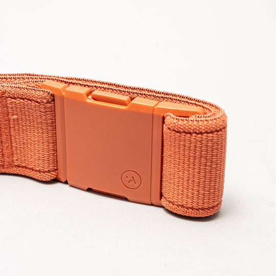 Close-up of the Atlas low profile belt by Arcade Belts in orange stretch webbing with a matching orange plastic buckle, featuring an embossed logo, shown on a plain white background.