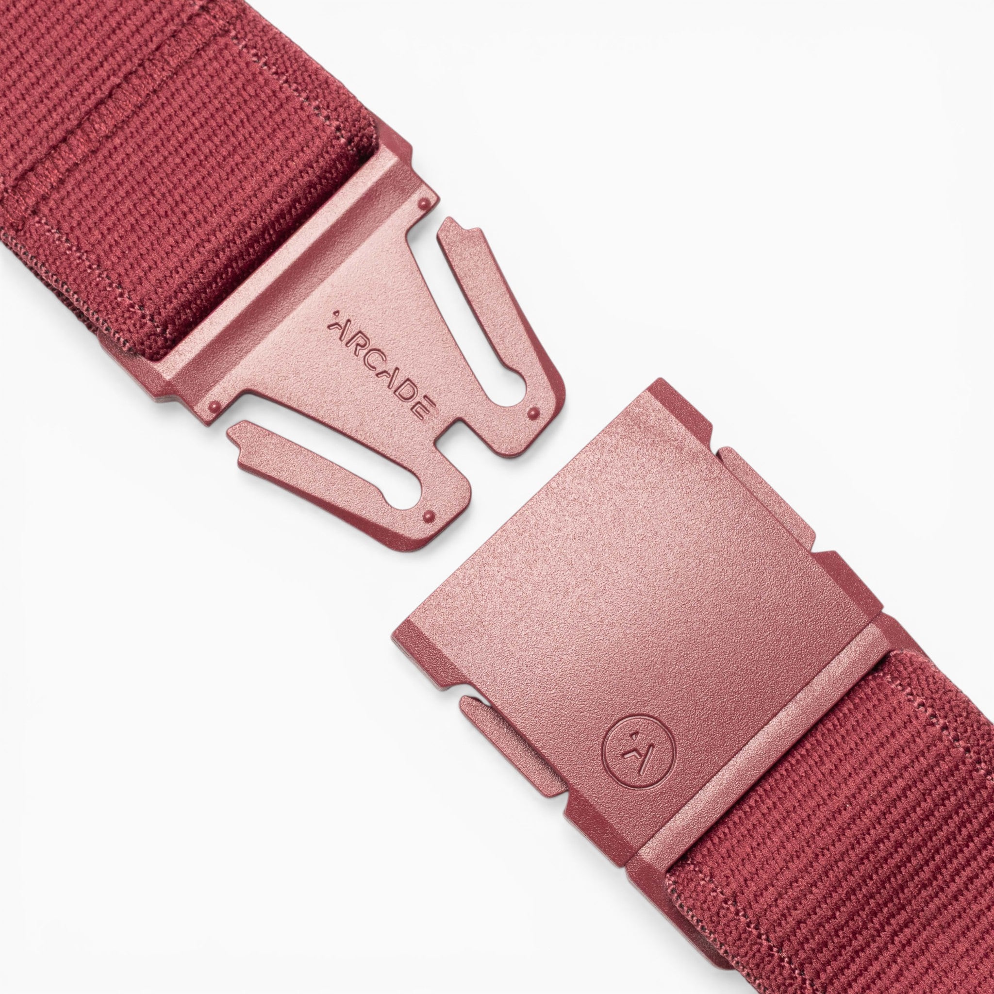 Close-up of the Atlas belt by Arcade Belts in red fabric, featuring a metal A2 buckle with “ARCADE” engraved on it. The buckle showcases a modern, angular design. The belt ends are positioned apart, ready to be fastened, highlighting the signature performance stretch construction of this Arcade Belts accessory.