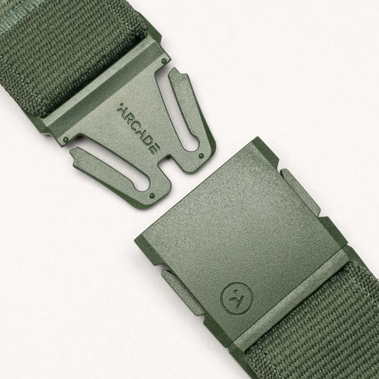 Close-up of the Atlas belt by Arcade Belts in green, featuring a woven strap and partially unclasped plastic A2 buckle. The buckle displays "ARCADE" on one side and a small logo on the other, set against a light neutral background.