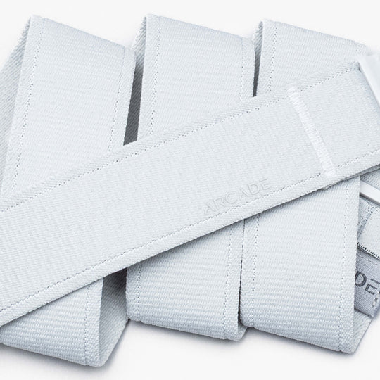 A close-up of the light gray Atlas performance stretch belt by Arcade Belts, featuring an A2 buckle and a subtle ARCADE emboss, folded in an overlapping pattern on a white background.