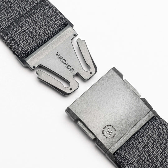 Close-up of the gray Atlas woven elastic stretch belt by Arcade Belts, featuring a metal clasp buckle. The partially open buckle shows ARCADE and a small logo on the metal against a white background.