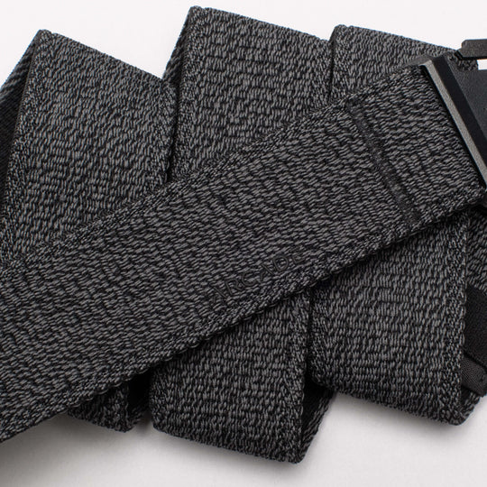 A close-up of the Atlas by Arcade Belts, a black and gray textured travel belt looped in several folds, with its low-profile black buckle partially visible on the right.