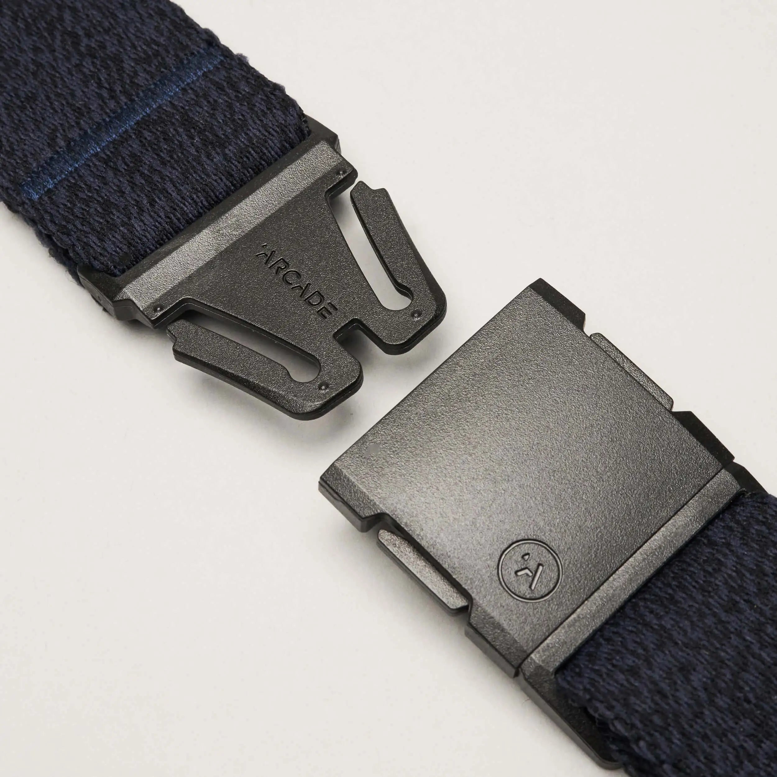 Close-up of a black metal buckle on the navy blue Atlas belt by Arcade Belts, partially unclasped with ARCADE engraved on the clasp, displayed against a plain white background.