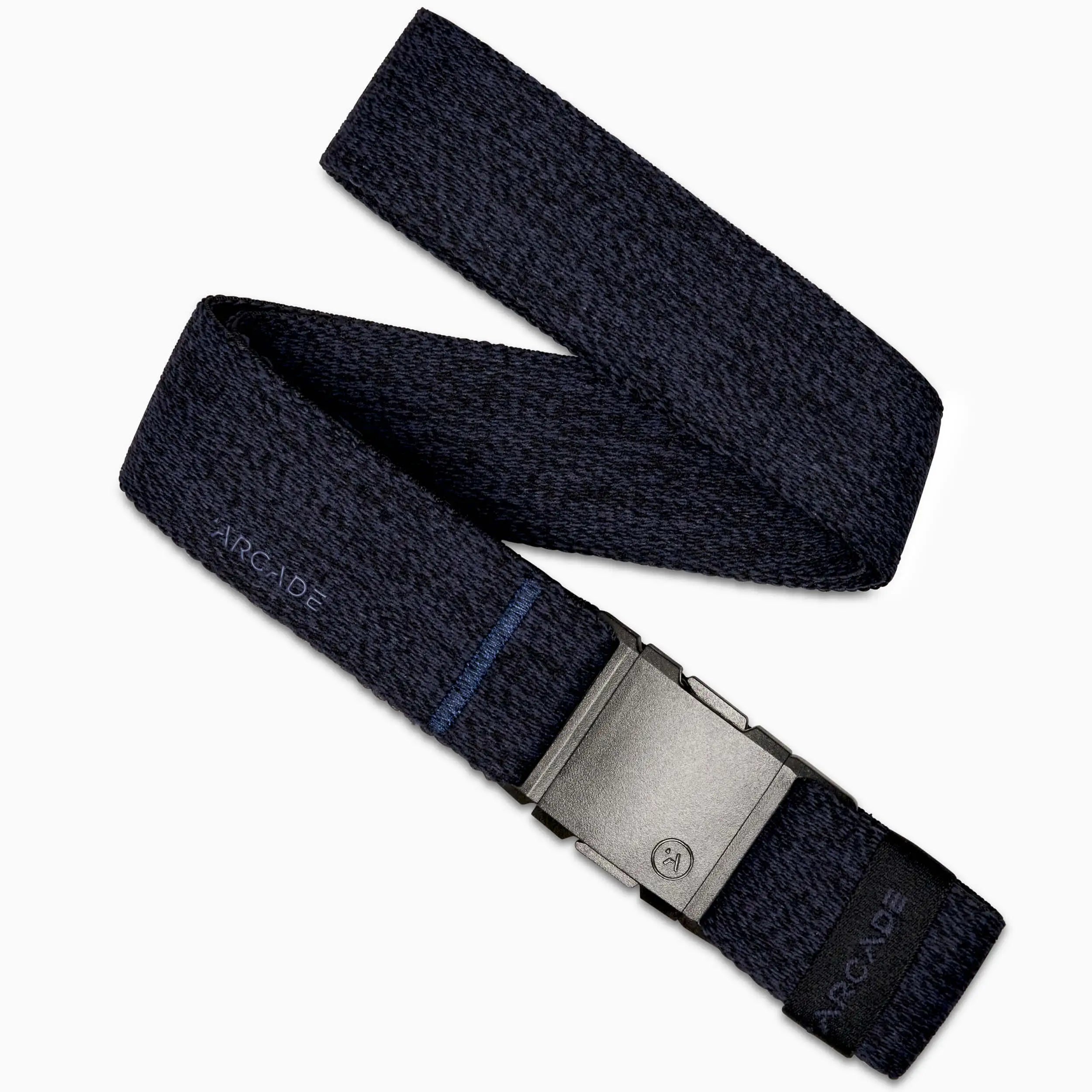 The Atlas by Arcade Belts is a dark blue elastic stretch belt with a gray rectangular low-profile buckle. ARCADE appears subtly near the buckle on this woven belt, shown laid out in a zigzag shape.