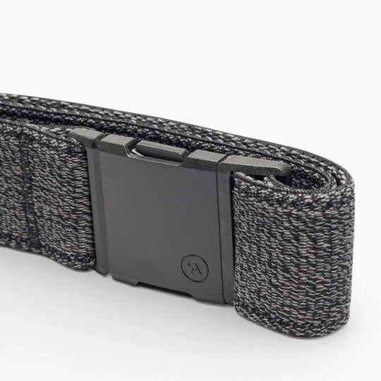 A close-up of the Atlas belt by Arcade Belts, showing its black elastic stretch design with a matte black rectangular buckle and a textured woven pattern with lighter gray threads, neatly folded on a white background.