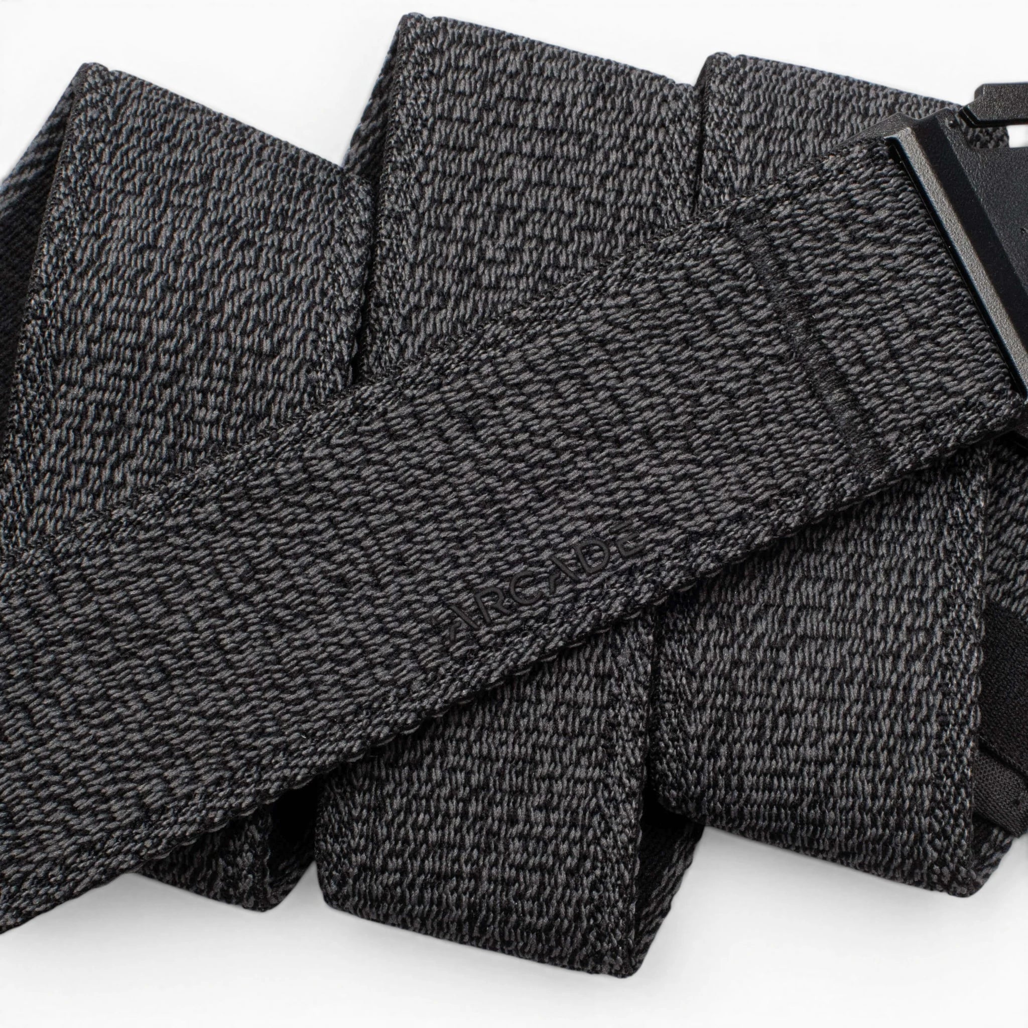A close-up of the Atlas by Arcade Belts, a black and gray textured travel belt looped in several folds, with its low-profile black buckle partially visible on the right.
