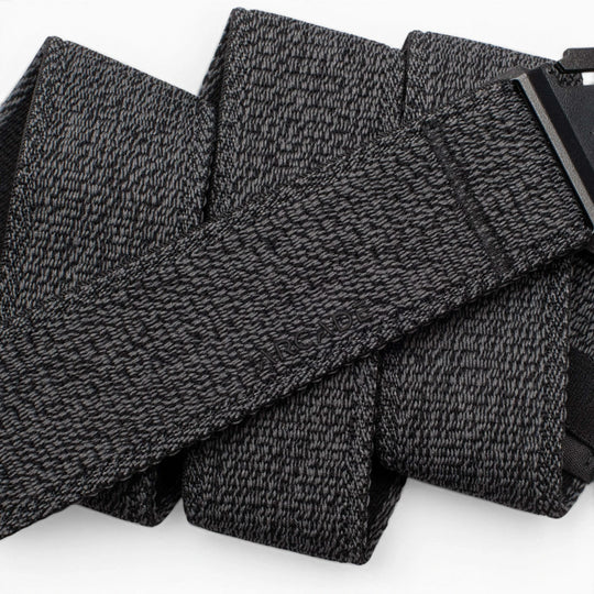 A close-up of the Atlas by Arcade Belts, a black and gray textured travel belt looped in several folds, with its low-profile black buckle partially visible on the right.