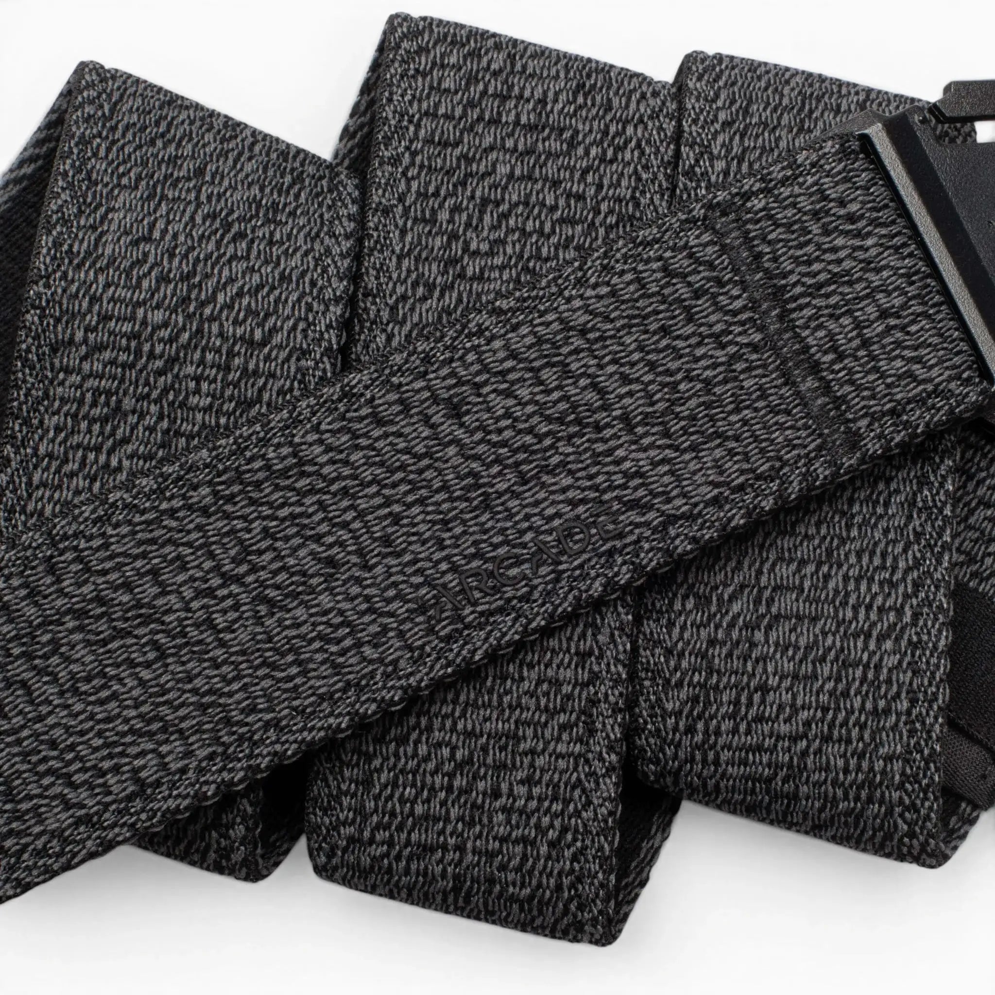 A close-up of the Atlas by Arcade Belts, a black and gray textured travel belt looped in several folds, with its low-profile black buckle partially visible on the right.