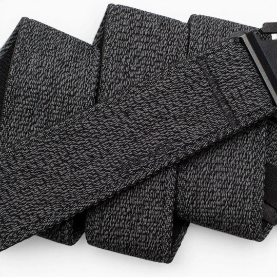 A close-up of the Atlas by Arcade Belts, a black and gray textured travel belt looped in several folds, with its low-profile black buckle partially visible on the right.