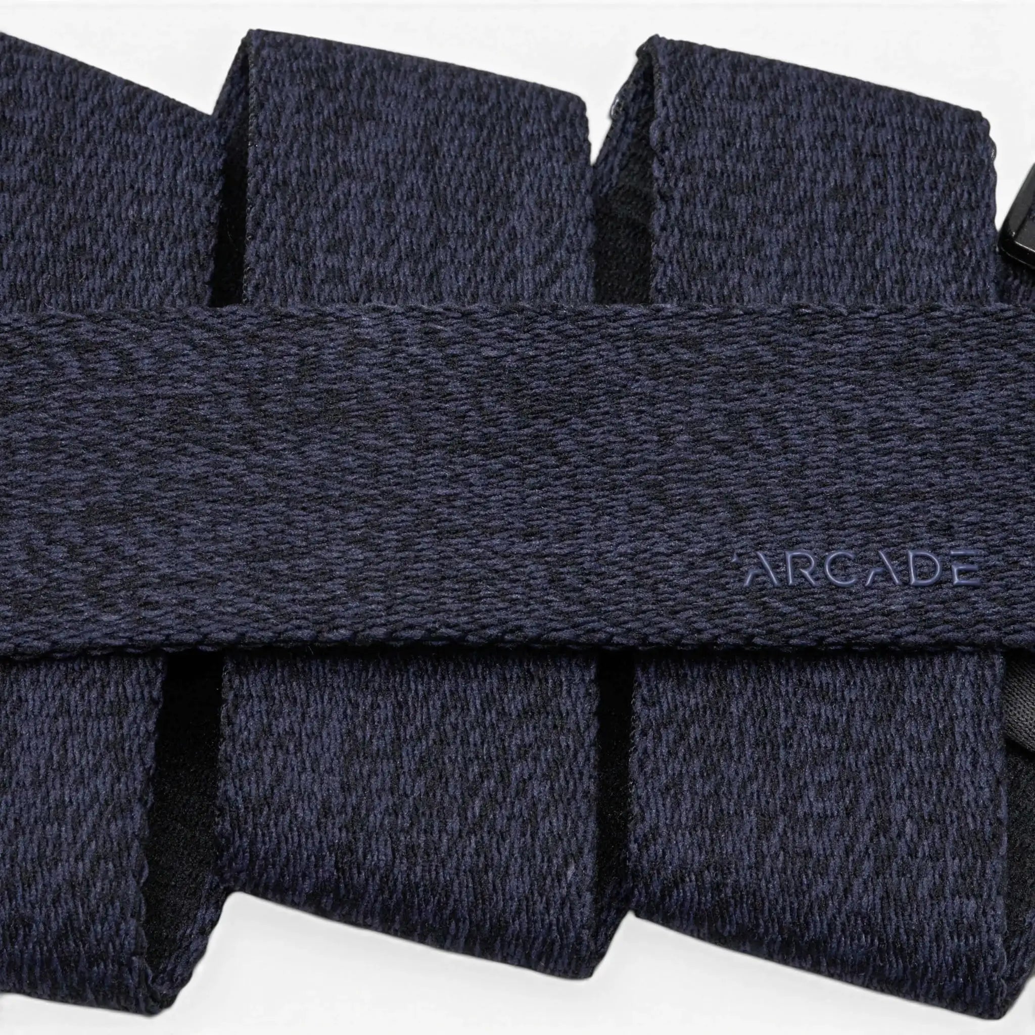 A close-up of a dark blue, textured Atlas belt by Arcade Belts with the brand name subtly printed in small, light blue letters on the surface.