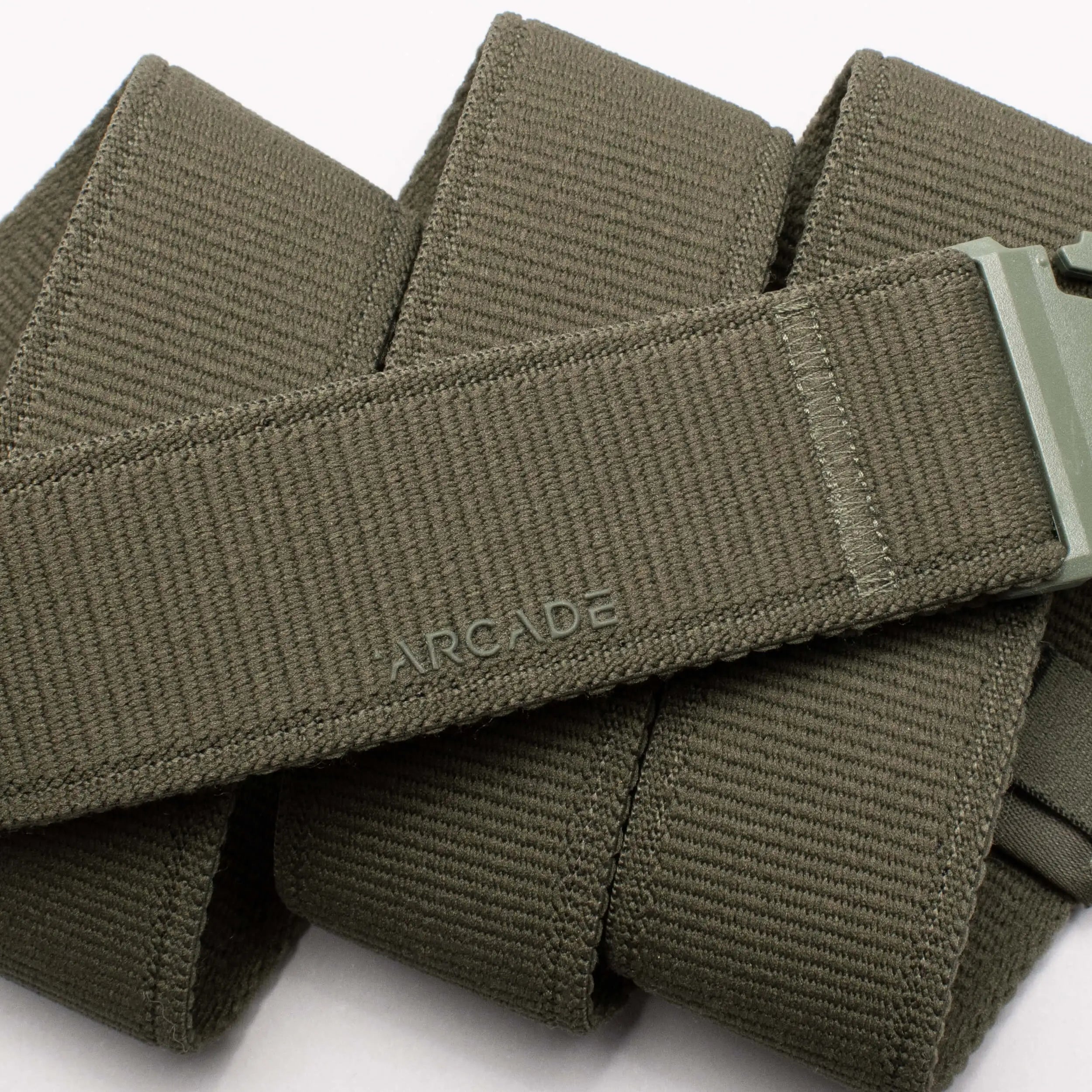 A close-up of the olive green Atlas Low Profile Belt from Arcade Belts, featuring a plastic buckle and the word ARCADE embossed on its surface—coiled neatly, its a stylish option for travel.