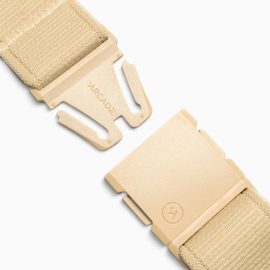 Close-up of the Atlas adventure belt by Arcade Belts in beige fabric, featuring a partially open plastic quick-release A2 buckle. One side of the buckle is engraved with “ARCADE,” while the other displays a small circular logo. Engineered for comfort and durability, this performance stretch belt is displayed against a white background.