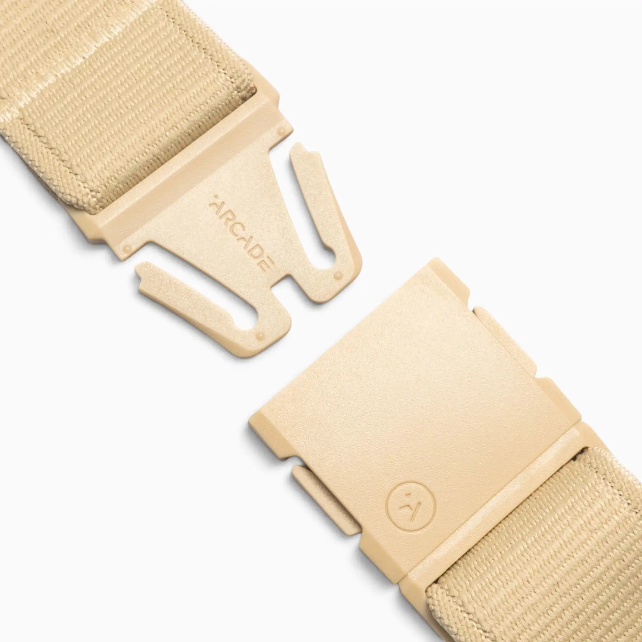 Close-up of the Atlas adventure belt by Arcade Belts in beige fabric, featuring a partially open plastic quick-release A2 buckle. One side of the buckle is engraved with “ARCADE,” while the other displays a small circular logo. Engineered for comfort and durability, this performance stretch belt is displayed against a white background.