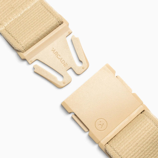 Close-up of the Atlas adventure belt by Arcade Belts in beige fabric, featuring a partially open plastic quick-release A2 buckle. One side of the buckle is engraved with “ARCADE,” while the other displays a small circular logo. Engineered for comfort and durability, this performance stretch belt is displayed against a white background.