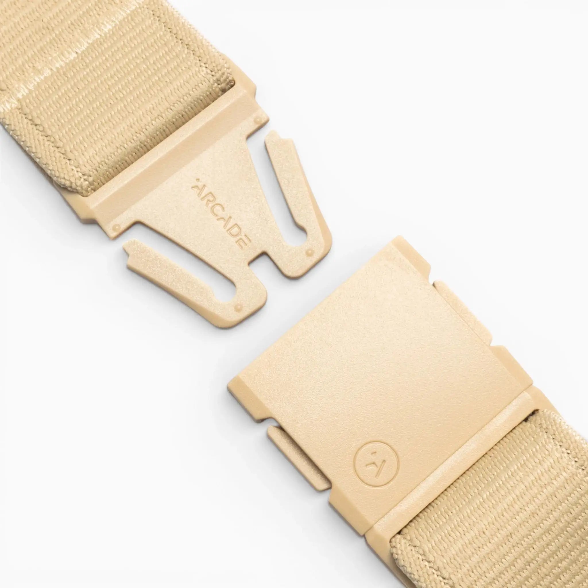 Close-up of the Atlas tan adjustable strap by Arcade Belts, featuring stretch webbing and a plastic buckle. The separated buckle shows the Arcade Belts logo and branding, all set against a light gray background.
