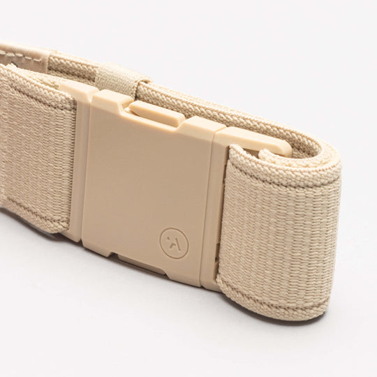 A close-up of a beige woven Atlas belt by Arcade Belts with a rectangular plastic buckle, featuring a small smiley face on the buckle, set against a plain white background.